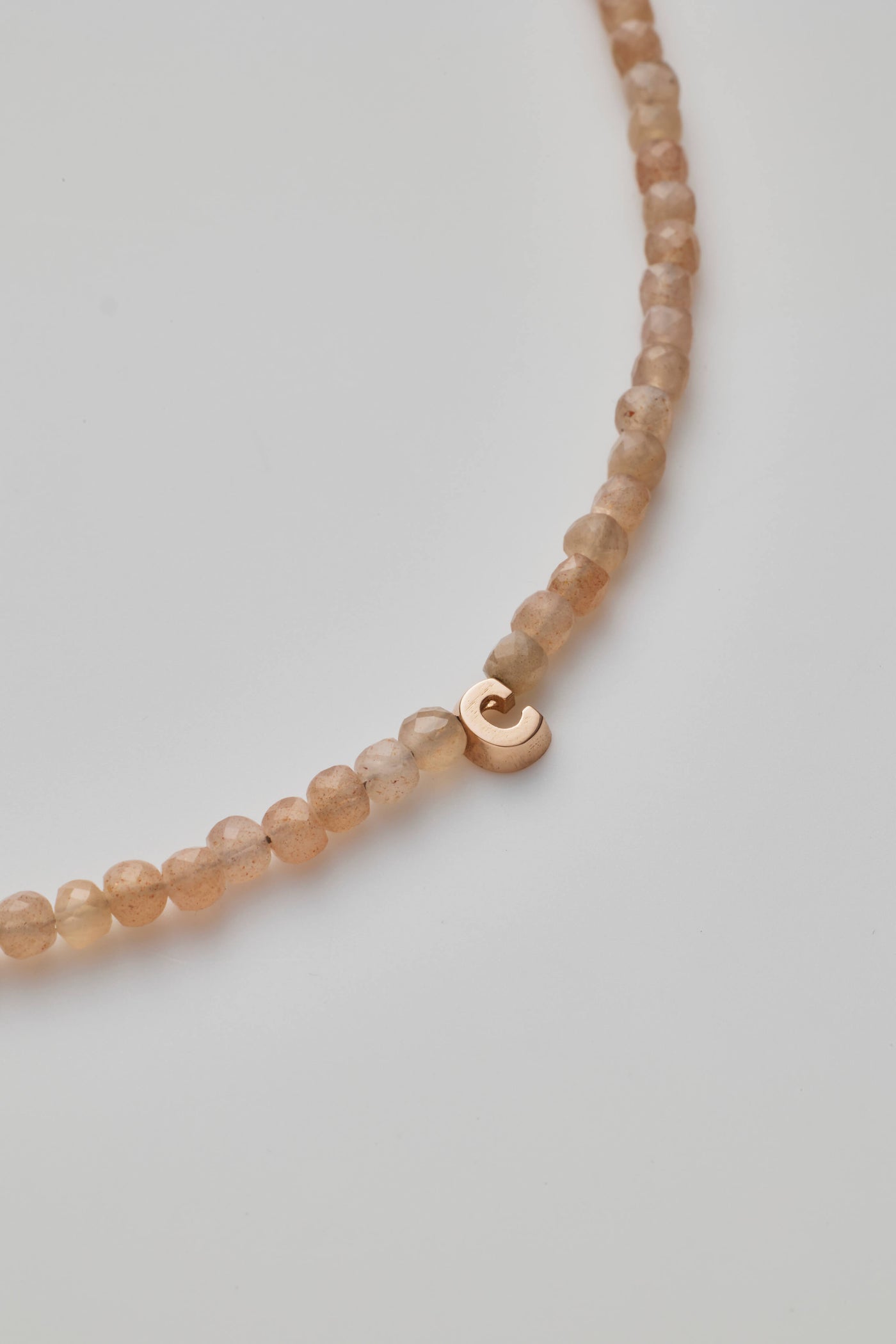 The One Letter Bracelet in Blush Moonstone and 14k Gold is a delicate, custom-sized piece featuring small, round blush moonstone beads evenly spaced along its length. The light beige hues of the moonstones add a soft elegance, while the 14-karat gold lobster clasp and findings provide a subtle yet refined touch to its simple design.