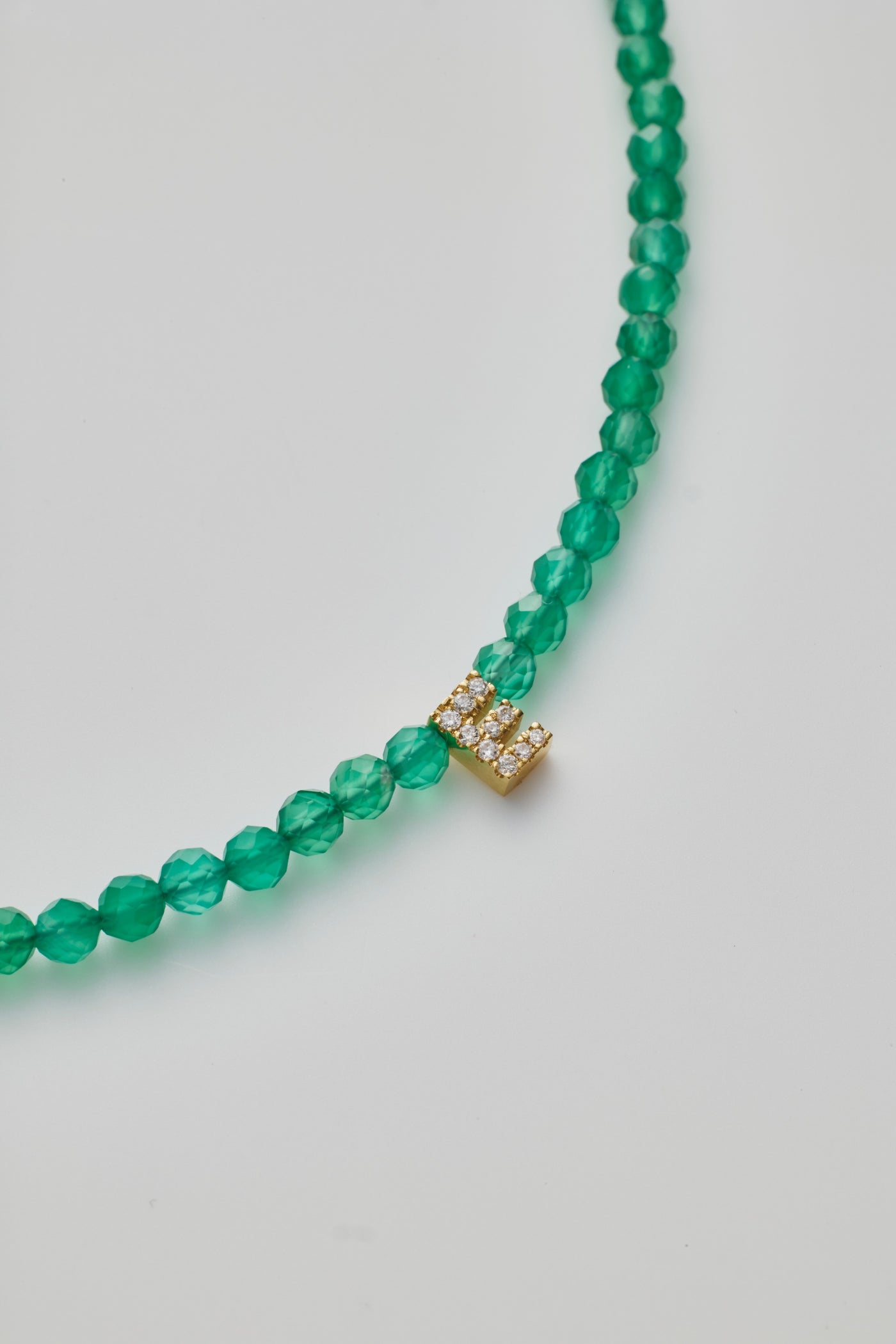 Delicate bracelet with green onyx beads and a diamond alphabet charm, elegantly crafted.