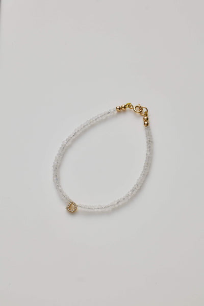 Delicate bracelet with moonstone beads and a diamond alphabet charm, elegantly crafted.