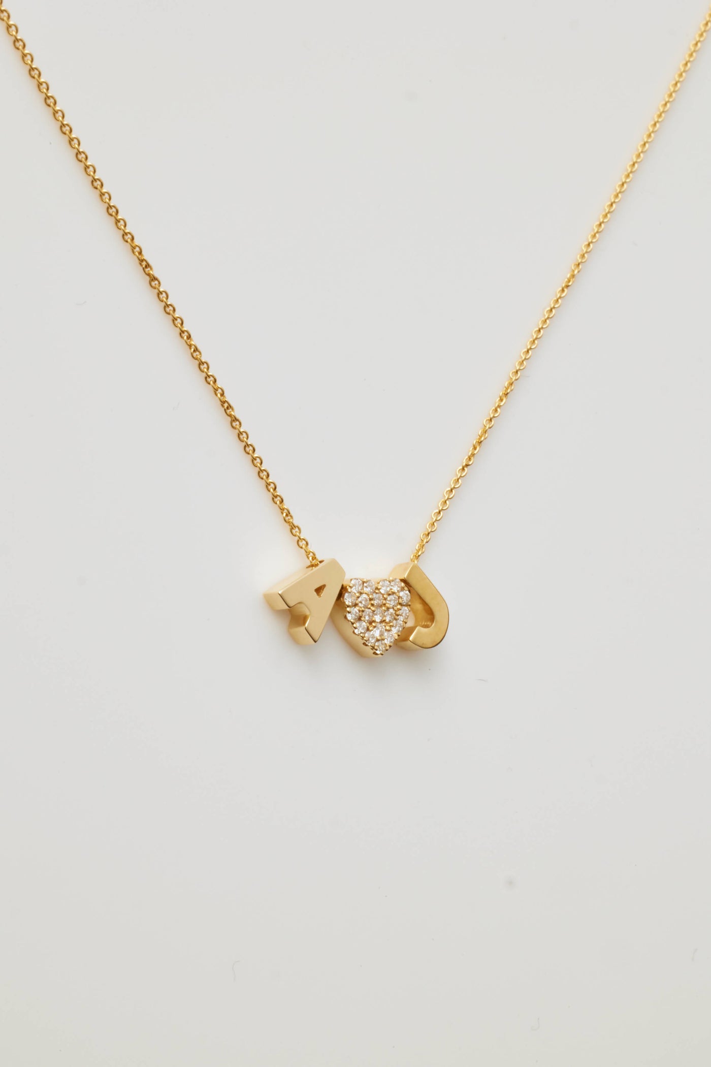 Introducing the Two Letters and Diamond Heart Necklace in 18k Gold: a delicate, solid gold piece that beautifully features the letters "A" and "J" alongside a heart-shaped charm embellished with small, sparkling diamonds nestled between them. Its thin and elegant chain flawlessly complements the minimalist design.