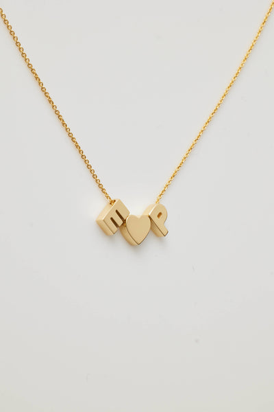 The Two Letters and Heart Necklace in 18k Gold boasts a delicate chain adorned with three exquisite charms: a capital letter "E" a heart symbol centrally placed, and a capital letter "P." Made from 18k solid gold, this beautiful piece is displayed against a simple, light-coloured backdrop and features an openable connector clasp for effortless wear.