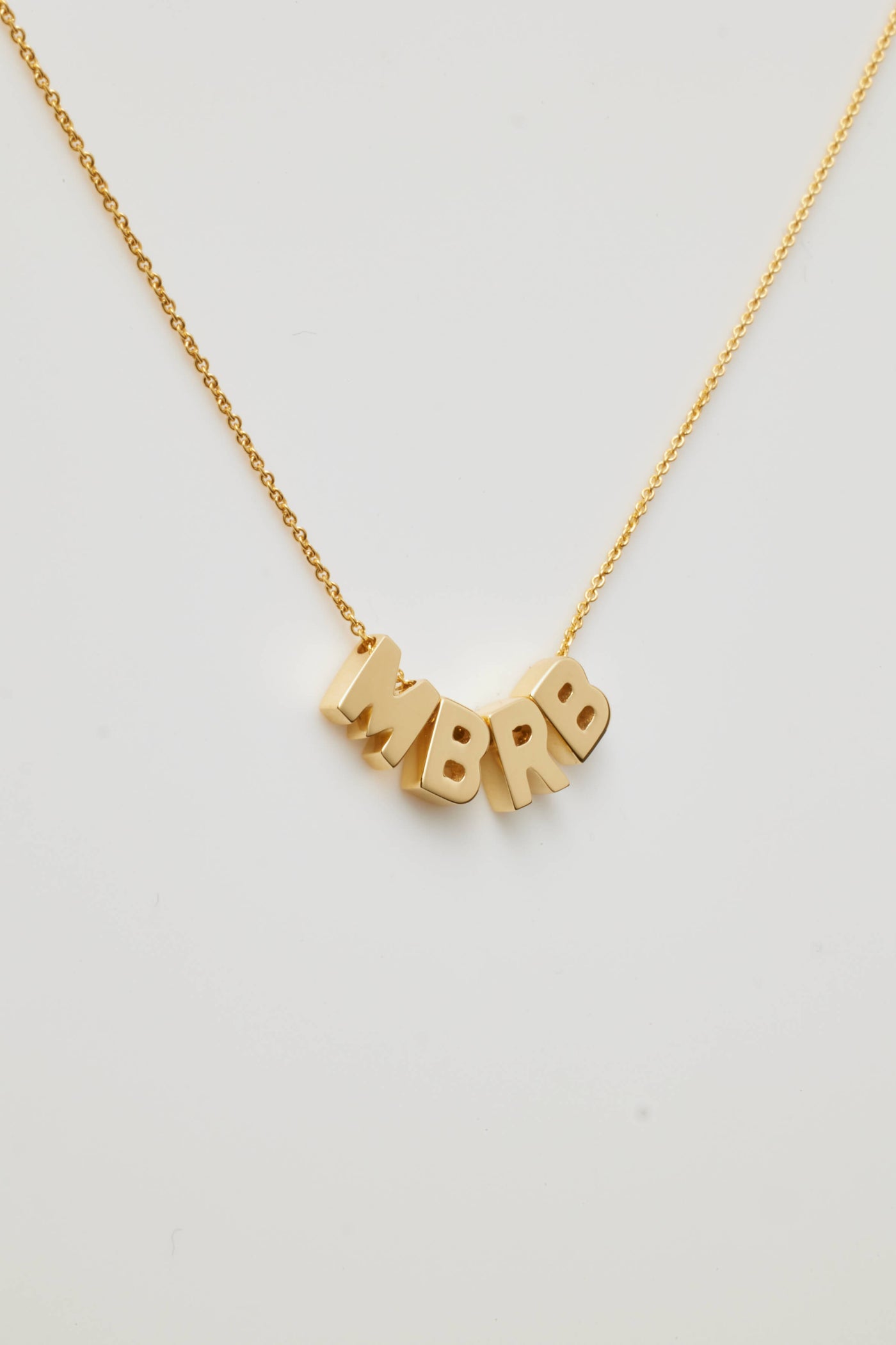 A delicate 18k solid gold necklace named the Four Letters Necklace in 18k Gold showcases a fine chain with letters MBRB letter charm pendants, elegantly displayed against a plain white background.