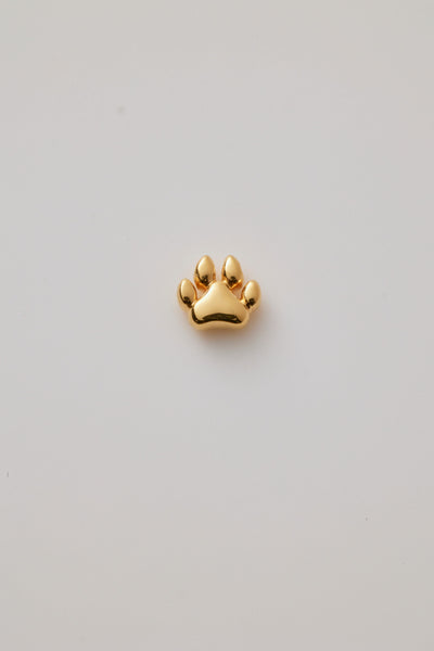 A polished gold dog paw charm with intricate detailing or raised paw pads on a light grey background.