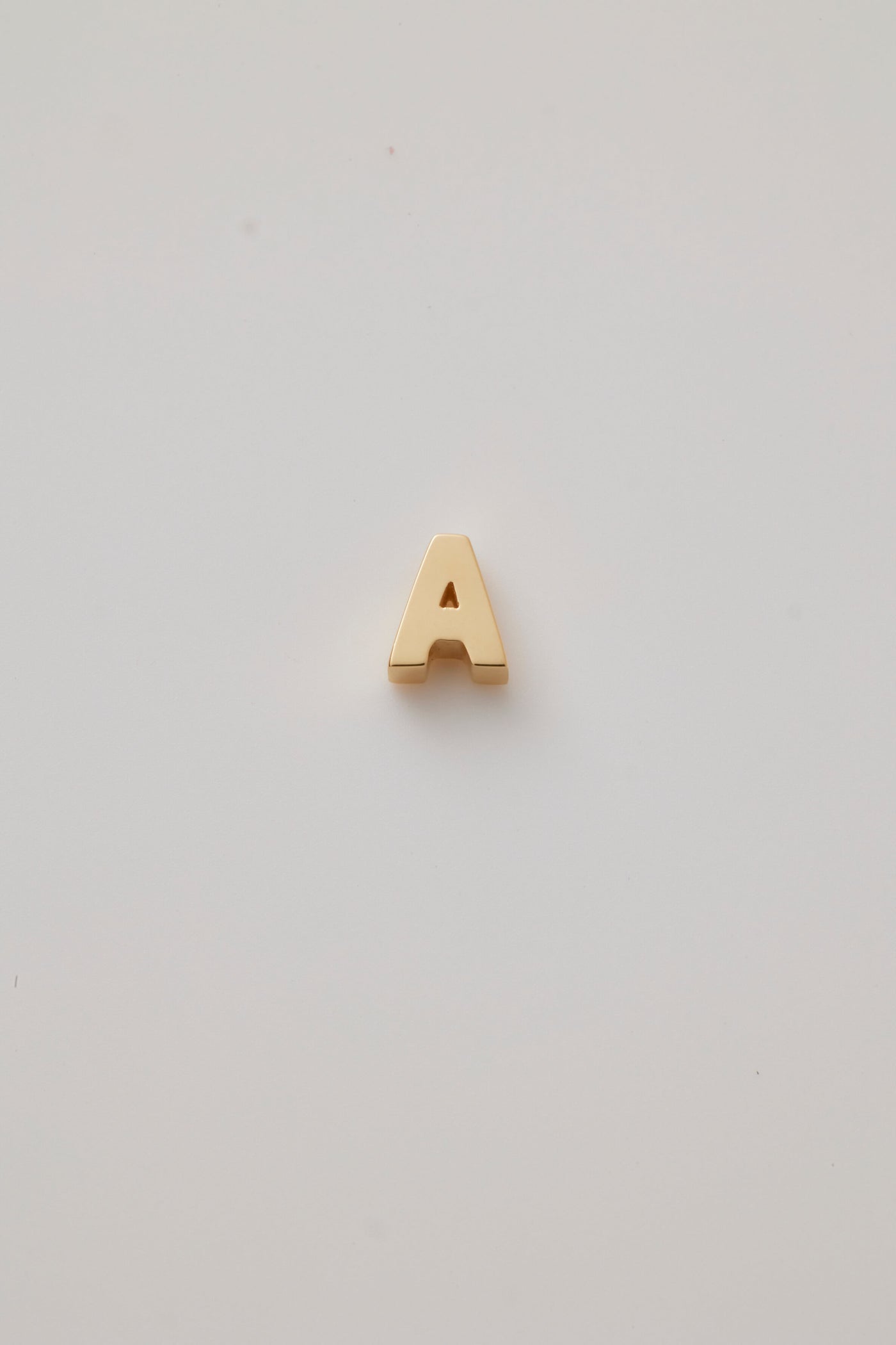 A three-dimensional charm crafted from 18-karat gold, shaped into a bold and elegant letter from the alphabet. The charm has a smooth, polished surface that gleams under light, highlighting its luxurious golden hue. Its edges are slightly rounded for a refined and sophisticated finish. The charm features a small, discreet hole at the top, allowing it to be easily attached to a chain or bracelet. The overall design is both modern and timeless, exuding a sense of opulence and personalisation.