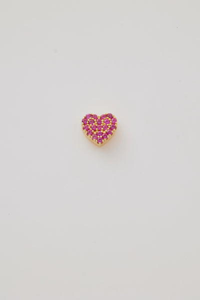 A solid gold miniature heart charm set with deep red ruby gemstones. The heart-shaped charm has a highly polished surface pavé-set in brilliant, vibrant rubies that add a touch of richness and elegance. A small gold hole at the top provides an easy attachment point for a chain or bracelet, making it a perfect accessory for a delicate and luxurious look.