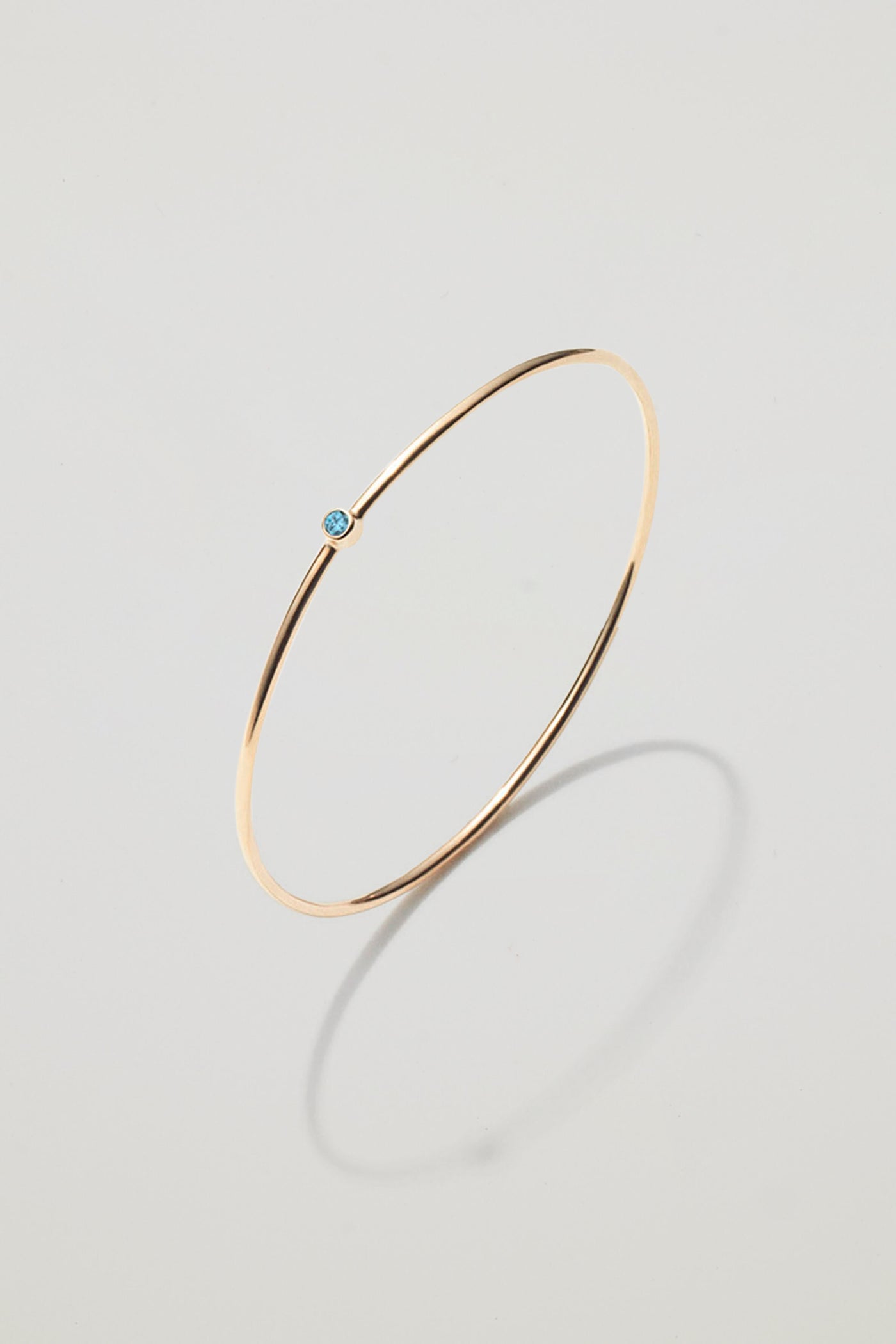 Solid gold bangle with a December blue topaz birthstone, symbolising peace and clarity.