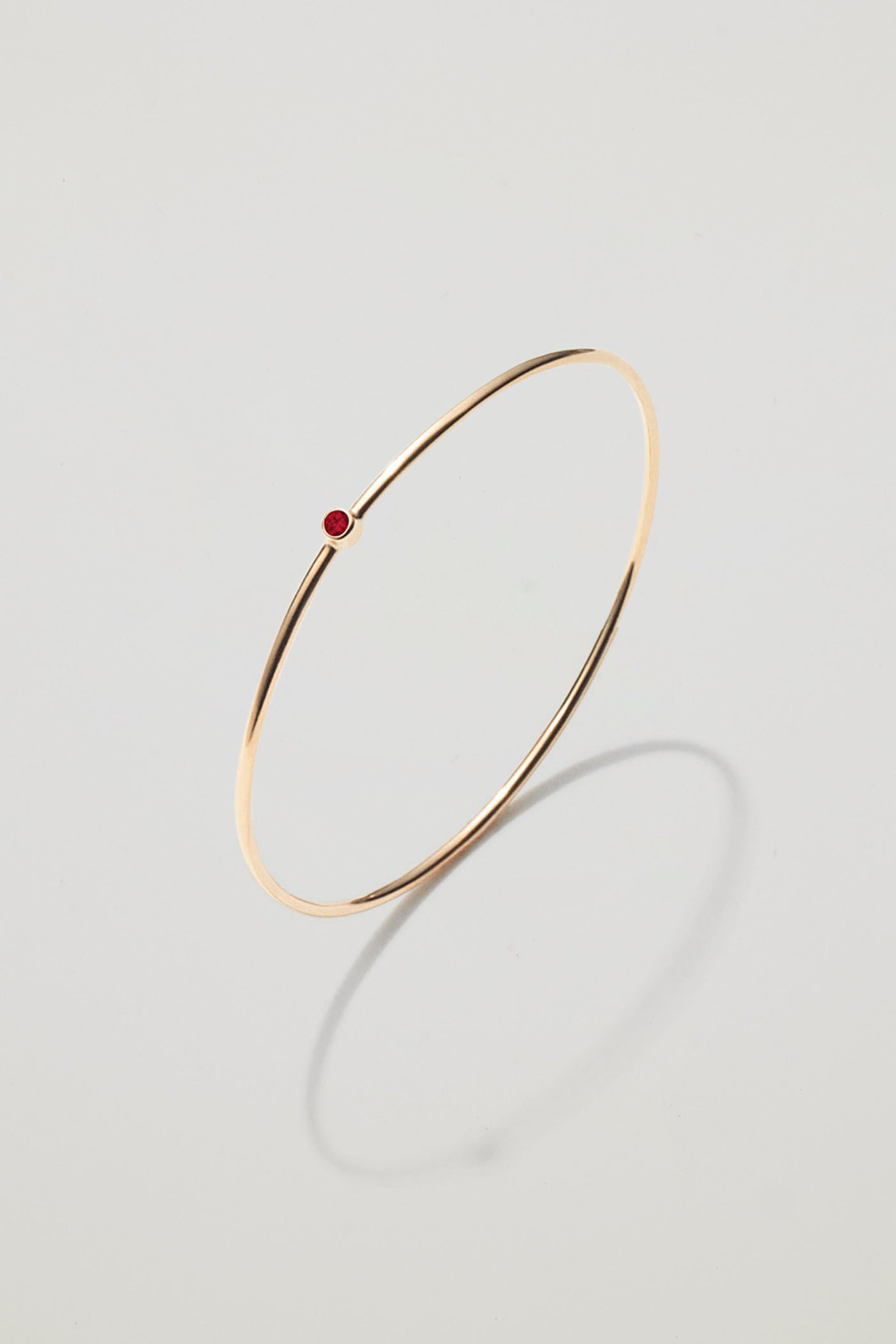 Solid gold bangle with a January garnet birthstone, symbolising strength and devotion.