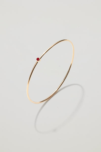 Solid gold bangle with a January garnet birthstone, symbolising strength and devotion.