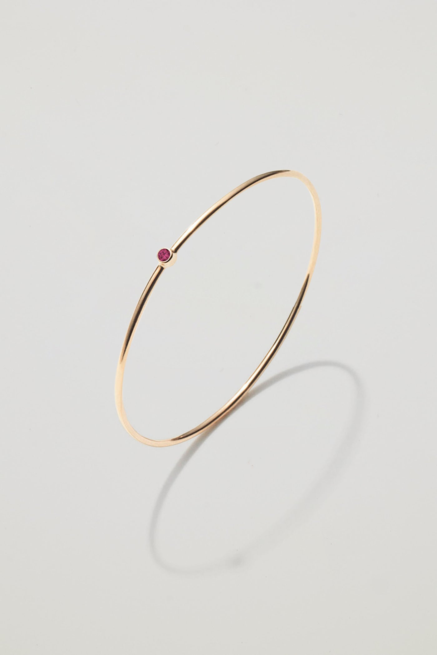Solid gold bangle with a July ruby birthstone, symbolising love and passion.