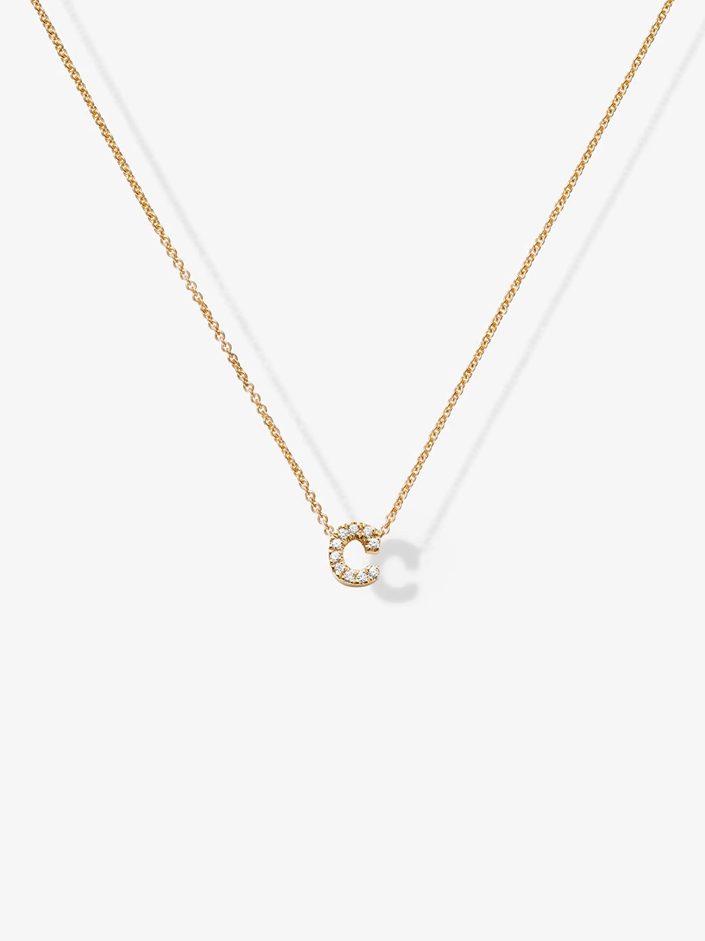 The Letter C Necklace in Diamonds and 18k Gold features a delicate 18k gold necklace with a small, sparkling diamond-encrusted pendant shaped like the letter "C." This exquisite diamond letter necklace hangs centrally on a customizable gold chain against a plain white background.