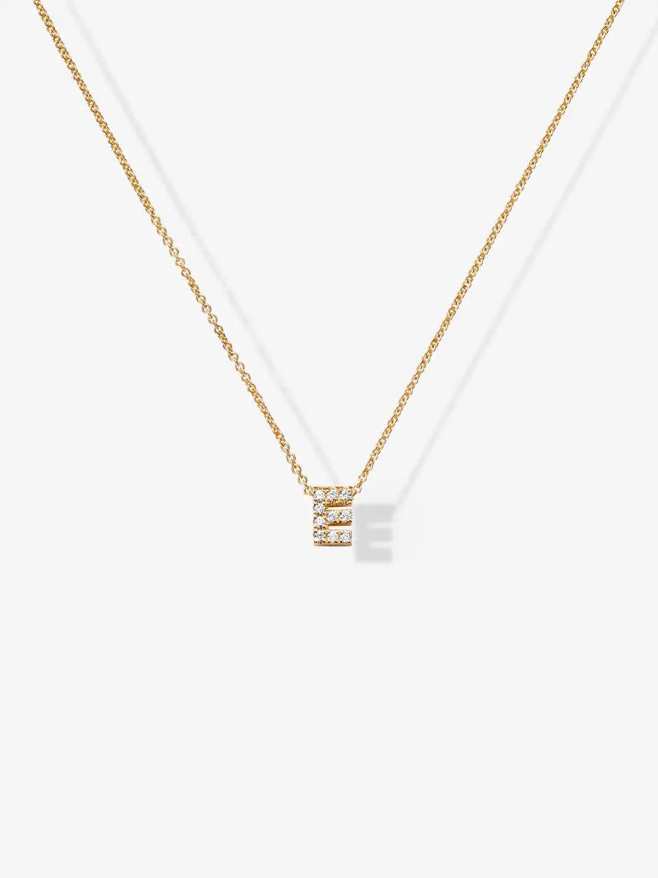 The "Letter E Necklace in Diamonds and 18k Gold" is a delicate piece of personalized jewelry featuring a small pendant shaped like the letter 'E,' adorned with tiny, sparkling diamonds against a plain white background. This exquisite necklace adds a touch of elegance to any ensemble.