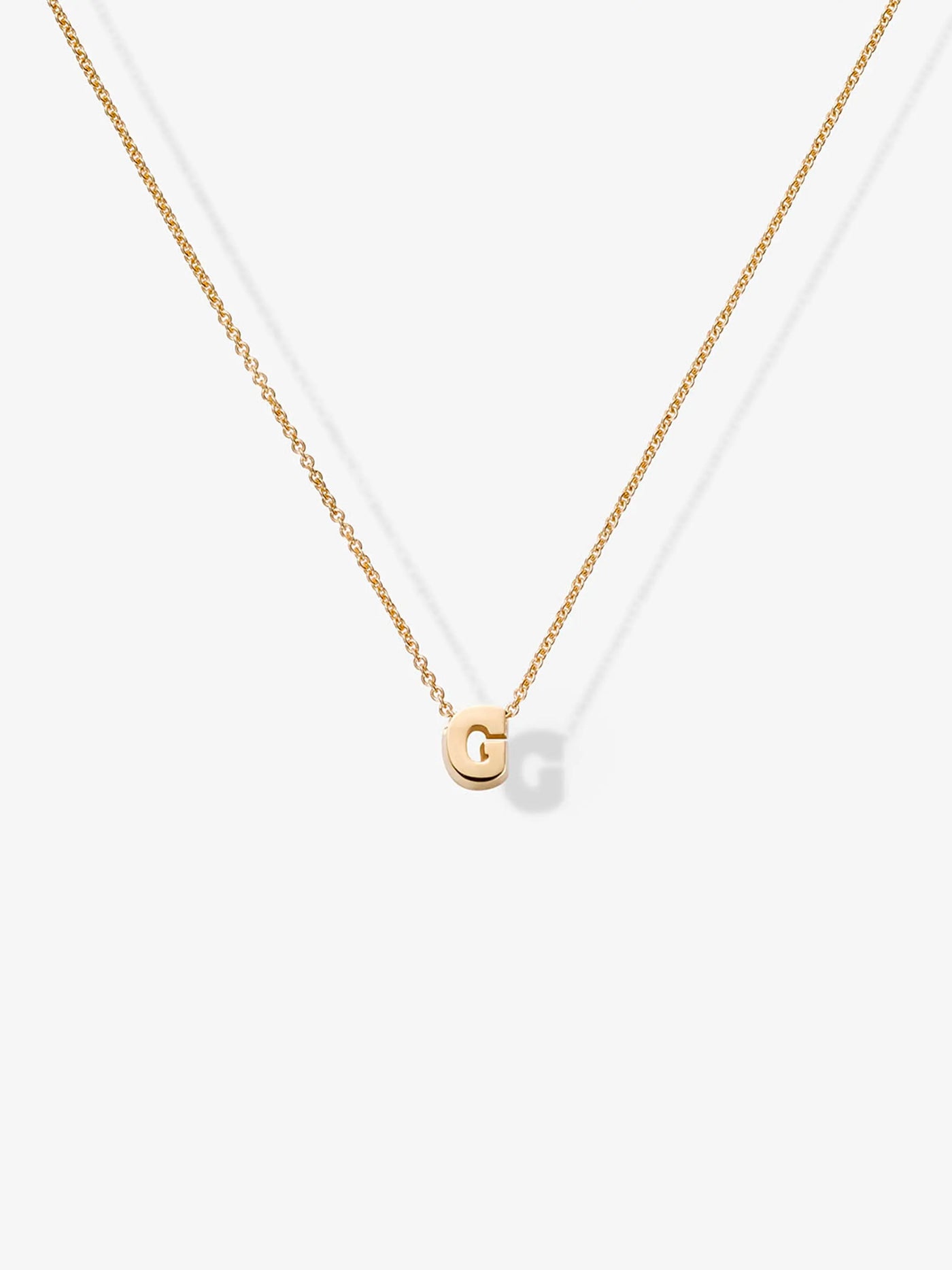 The Letter G Necklace in 18k Gold features a delicate and minimalistic design, showcasing a thin chain with a small gold pendant shaped like the letter 'G.' The elegant pendant rests at the center of the necklace, perfectly highlighted against a plain white background.