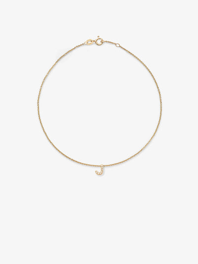 The "Letter J Bracelet in Diamonds and 18k Gold" is a delicate piece featuring an 18k solid gold chain adorned with a small pendant shaped like the letter "J" and encrusted with tiny round brilliant diamonds. The bracelet is equipped with a simple clasp closure and is displayed against a plain white background.