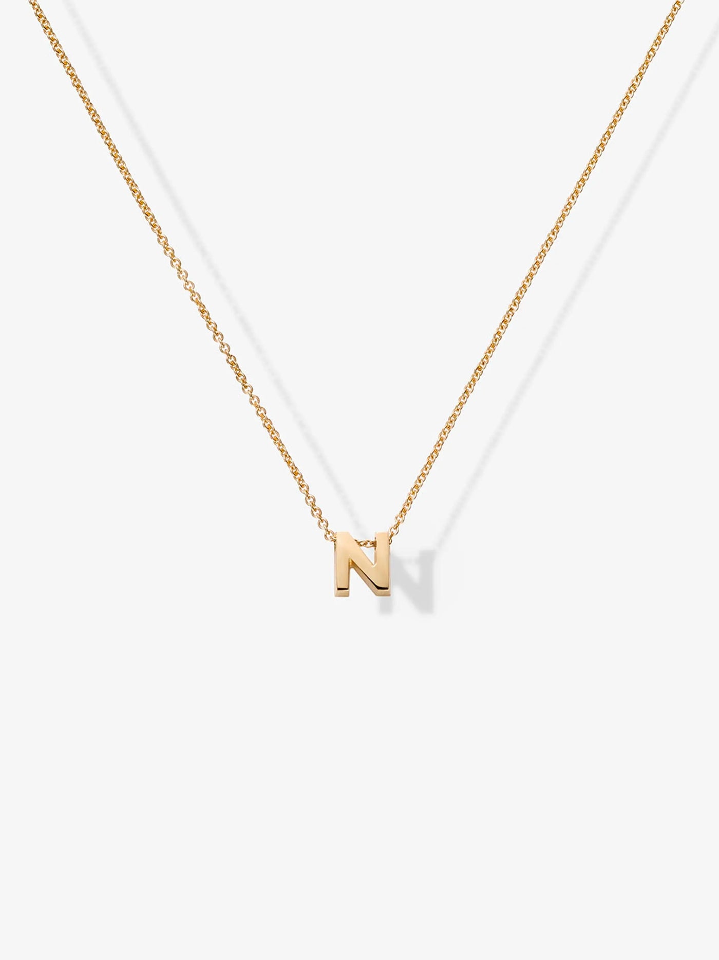 A thin, 18k solid gold necklace features a chain with a single "N" pendant, highlighting both simplicity and elegance against a plain white background. This signature piece is aptly named the Letter N Necklace in 18k Gold.