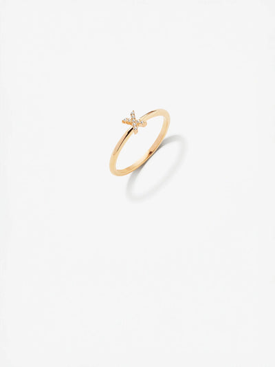 A delicate 18k solid gold "Letter X Ring" features a small, captivating butterfly design at its center. Adorned with tiny, sparkling round brilliant diamonds, the butterfly adds a touch of elegance. The ring casts a soft shadow on the light background.