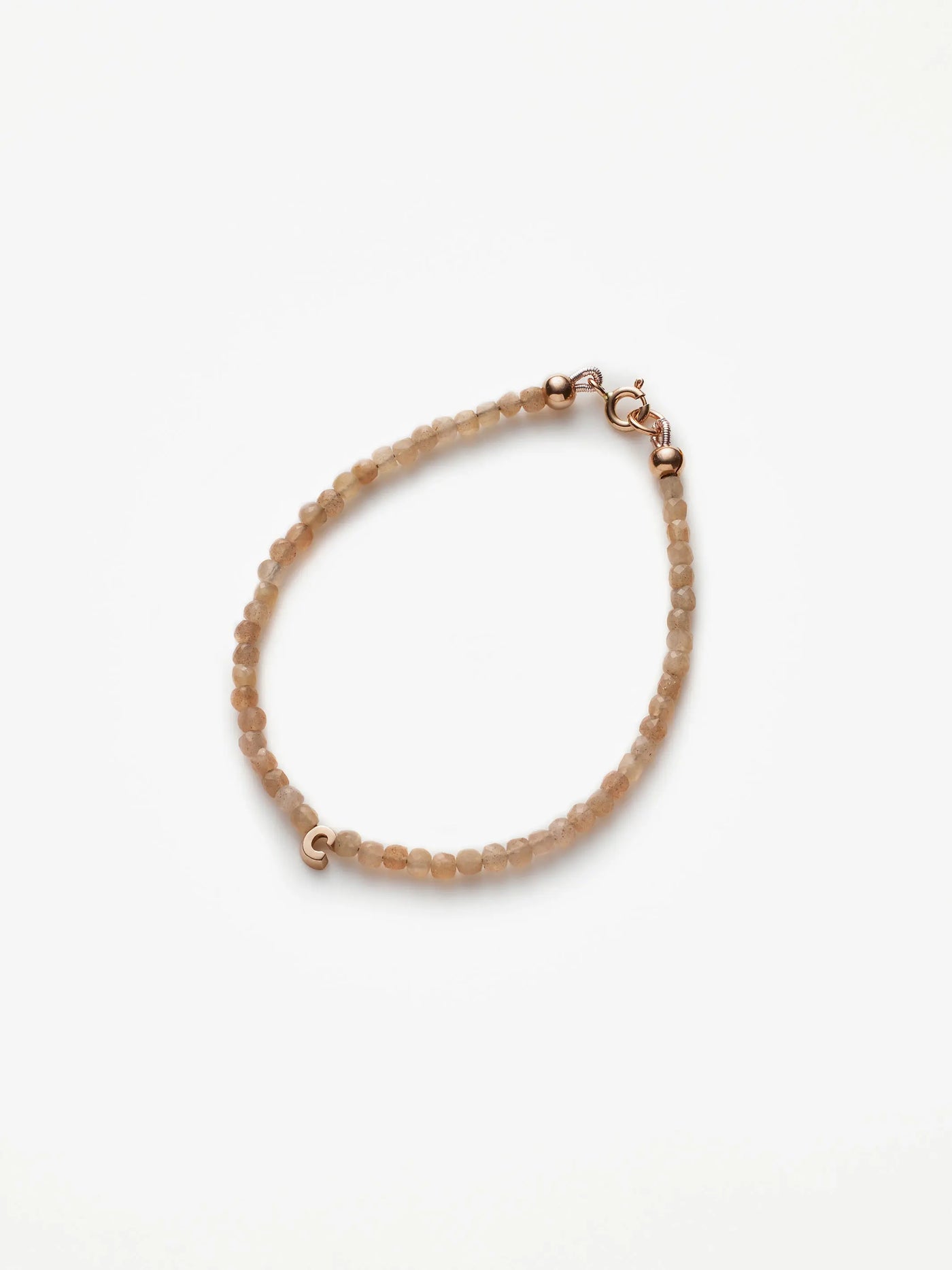 The One Letter Bracelet in Blush Moonstone and 18k Gold is a delicate, custom-sized piece featuring small, round blush moonstone beads evenly spaced along its length. The light beige hues of the moonstones add a soft elegance, while the 18-karat gold lobster clasp and findings provide a subtle yet refined touch to its simple design.