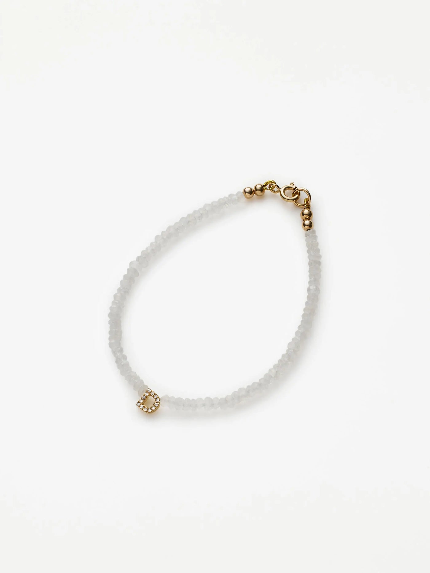 A delicate white beaded bracelet, the One Letter Bracelet in Diamonds, Rainbow Moonstone and 18k Gold, showcases a small solid gold charm and clasp. The round moonstone beads exude elegance with the added sparkle of diamonds. Set against a plain white background, its simplicity and beauty are highlighted perfectly.