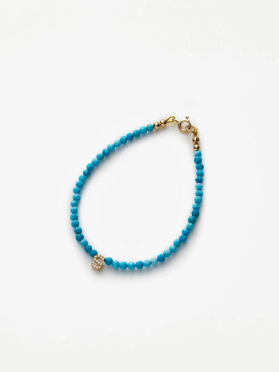 The One Letter Bracelet in Diamonds, Turquoise and 18k Gold is a delicate piece made of small turquoise beads, featuring an 18k solid gold clasp and a central gold charm adorned with tiny white gemstones. Arranged in a circular shape on a plain white background, this bracelet is perfect for any occasion.