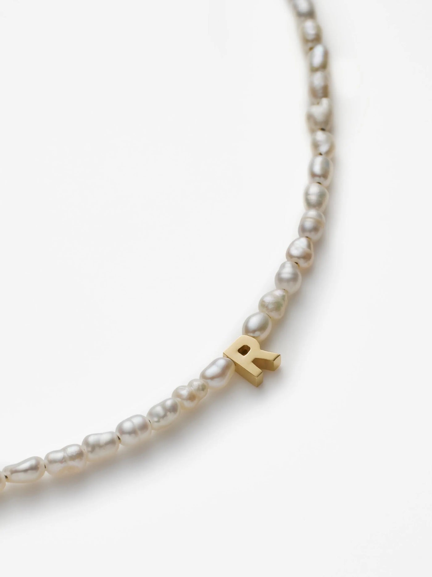 The One Letter Bracelet in Pearl and 18k Gold is a delicate piece featuring small pearls and a central gold letter "R" charm, elegantly showcased against a plain white background. Custom sizes and 18k gold options are available to ensure the perfect fit.