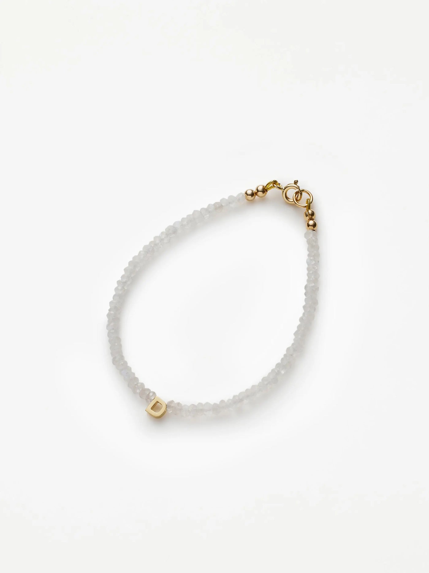 The One Letter Bracelet in Rainbow Moonstone and 18k Gold features small, translucent beads with a single 18k solid gold bead displaying the letter "D." This elegant bracelet includes a gold clasp closure and can be customized to fit different sizes. The product is showcased against a plain white background.