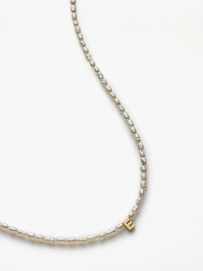 The One Letter Necklace in Pearl and 18k Gold showcases an exquisite array of irregularly shaped freshwater pearls. Near the bottom of the necklace, a small 18k gold charm, featuring a letter "E," is elegantly integrated into the design. The necklace is displayed on a plain white background.