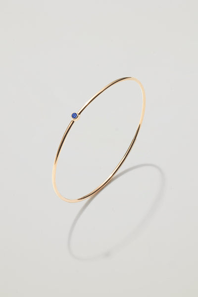 Solid gold bangle with a September sapphire birthstone, symbolising loyalty and wisdom.