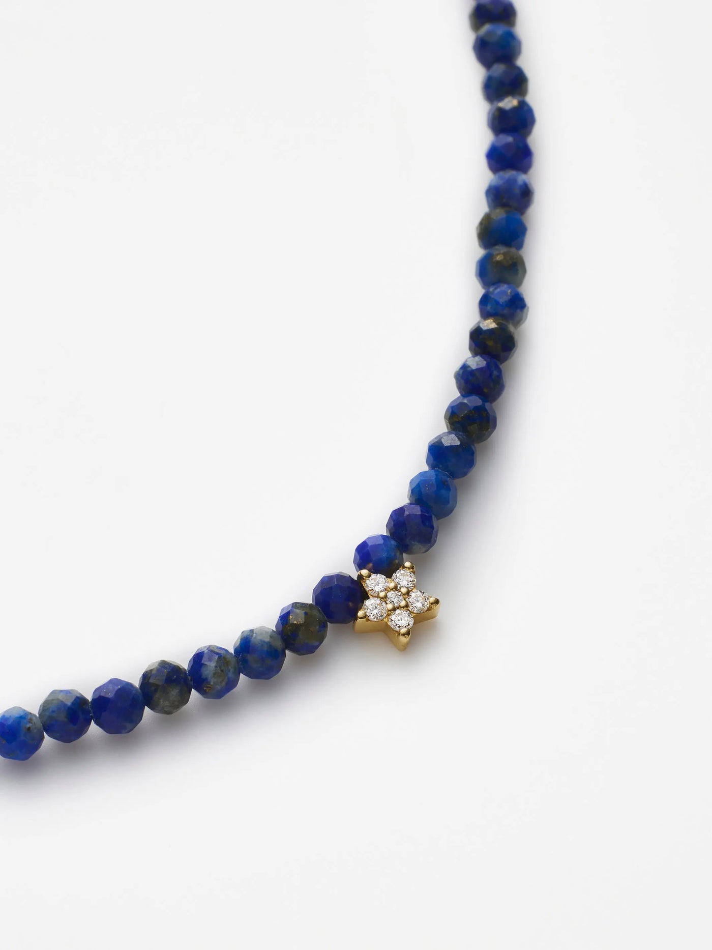 Introducing the Star Bracelet in Diamonds, Lapis Lazuli and 18k Gold: a beaded lapis lazuli bracelet adorned with small blue stones, featuring an 18k solid gold clasp and a sparkling diamond star charm. It boasts a simple yet elegant design, beautifully showcased against a plain white background.