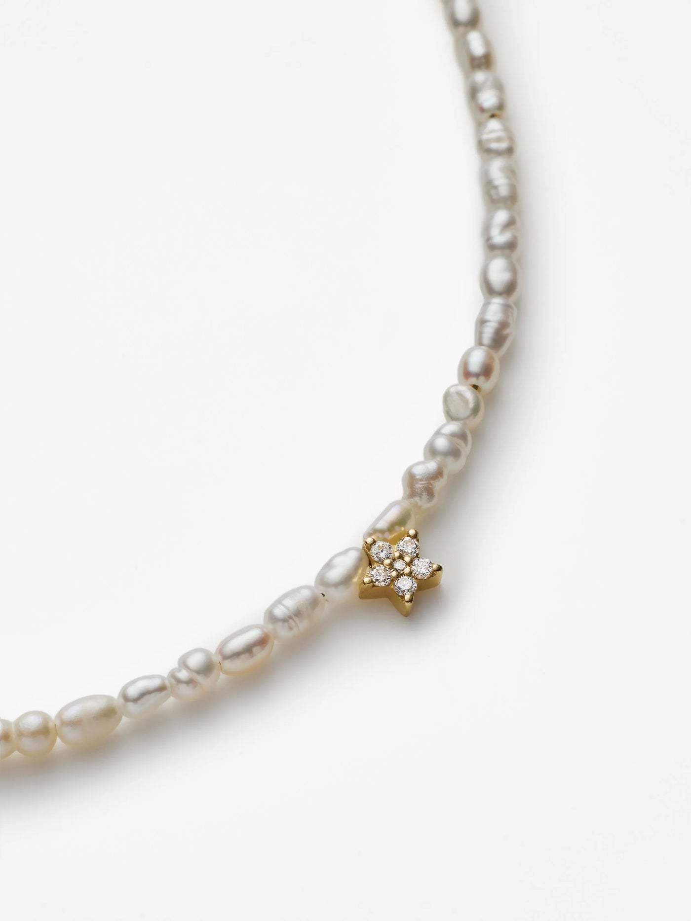 The Star Bracelet in Diamonds, Pearl, and 18k Gold is a delicate accessory featuring a strand of small, white freshwater pearls. It showcases a tiny gold flower charm adorned with a small pearl at its center. Crafted from 18k solid gold, this bracelet is secured with a small gold clasp, while the white background accentuates its elegance.