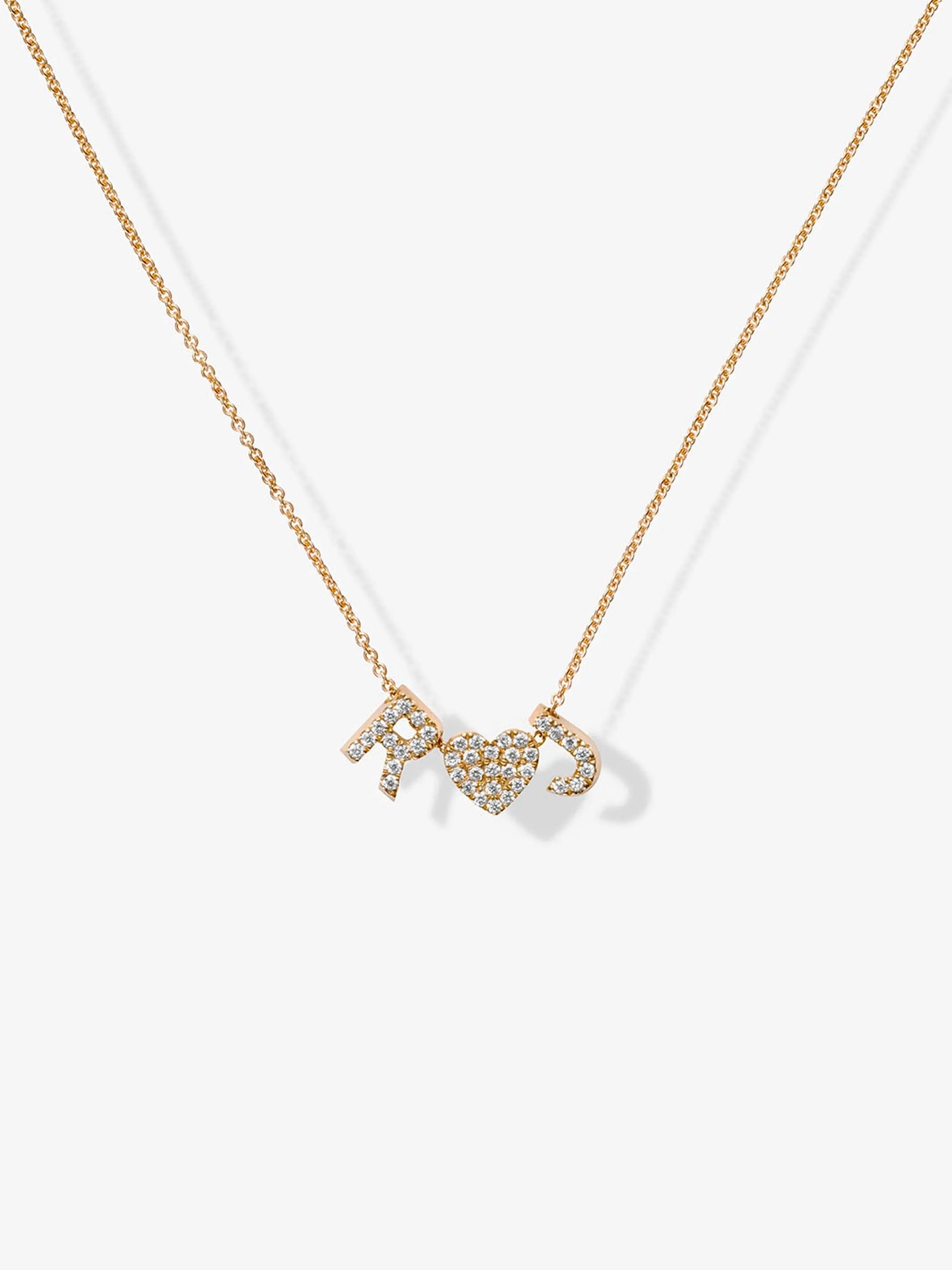 The Two Letters and Heart Necklace in Diamonds and 18k Gold showcases a delicate 18k solid gold chain adorned with three charm pendants: the letters "R" and "C" embellished with small, shimmering diamonds, and a central heart charm adorned with matching diamonds. This elegant piece boasts a minimalist chain without other decorations.