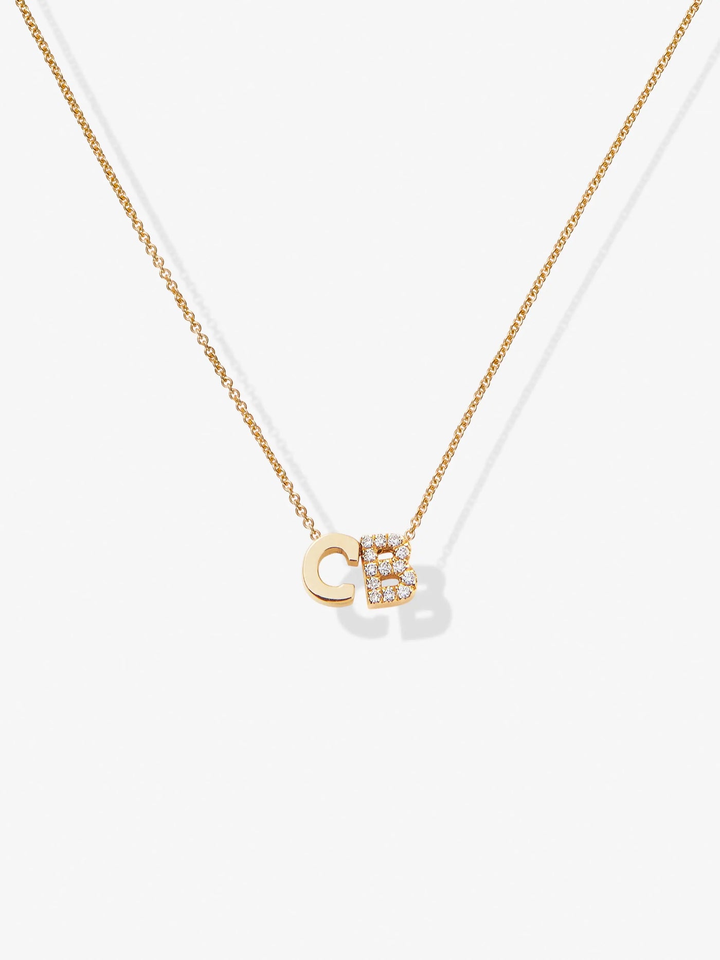 The Two Letters Necklace in Diamonds and 18k Gold showcases a minimalist and elegant design with two hanging pendants: a solid 18k gold "C" and a gold "B" encrusted with sparkling diamonds. This stunning necklace shines beautifully against a plain white background.