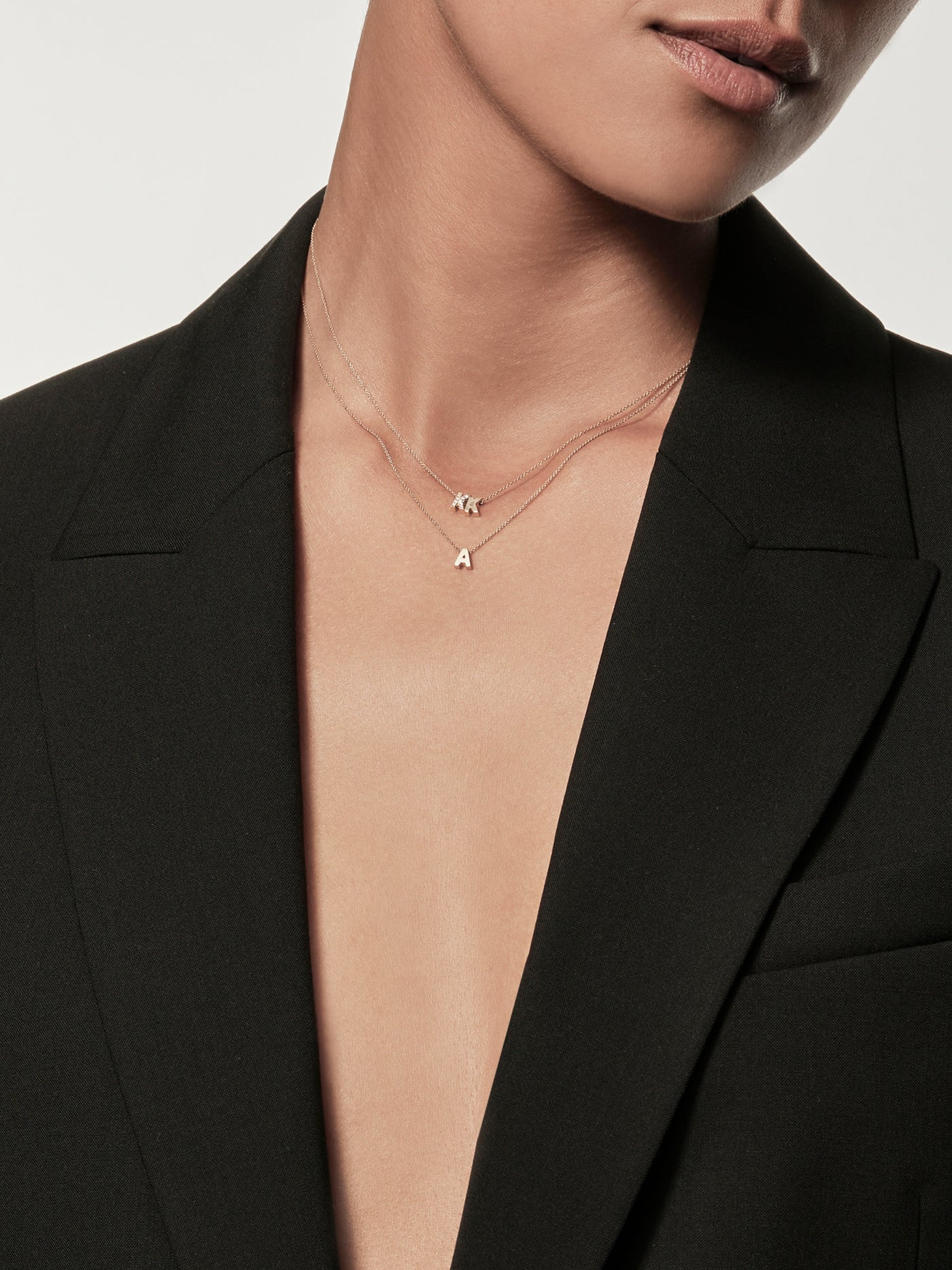 Close-up of a woman wearing a black blazer and a delicate necklace with gold miniature letter pendants.
