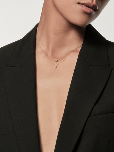Close-up of a woman wearing a black blazer and a delicate necklace with gold miniature letter pendants.