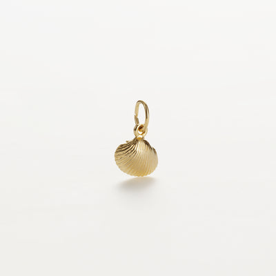 The Shell Charm in 9k Gold is a small charm shaped like a scallop shell, featuring a polished surface and fine ridges. It is displayed against a plain white background and includes a small loop at the top, suitable for attaching to bracelets or necklaces.