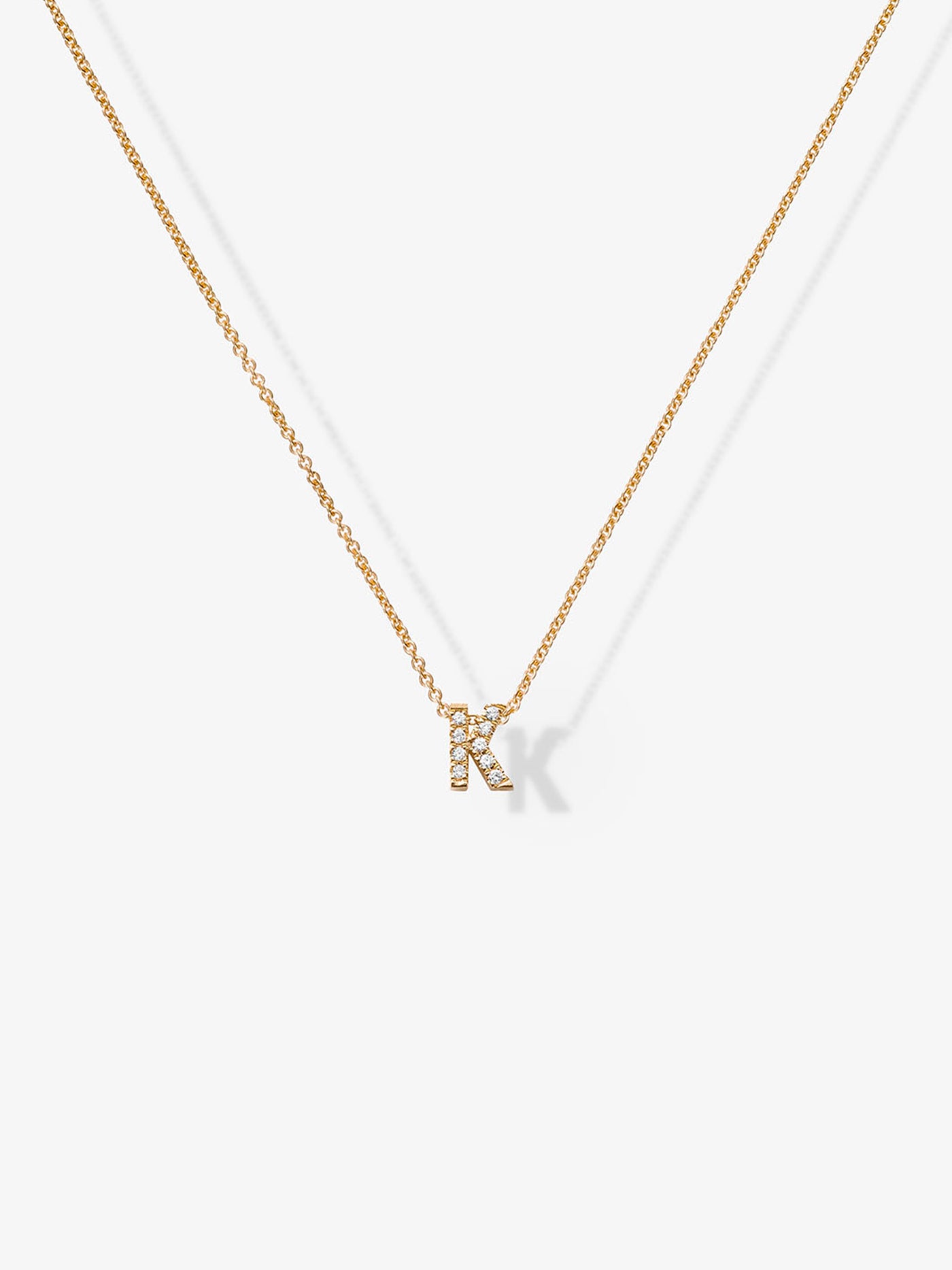 A finely crafted piece, the Letter K Necklace in Diamonds and 18k Gold showcases a delicate solid gold chain featuring a small "K" pendant adorned with shimmering gemstones, all set against a plain white background.