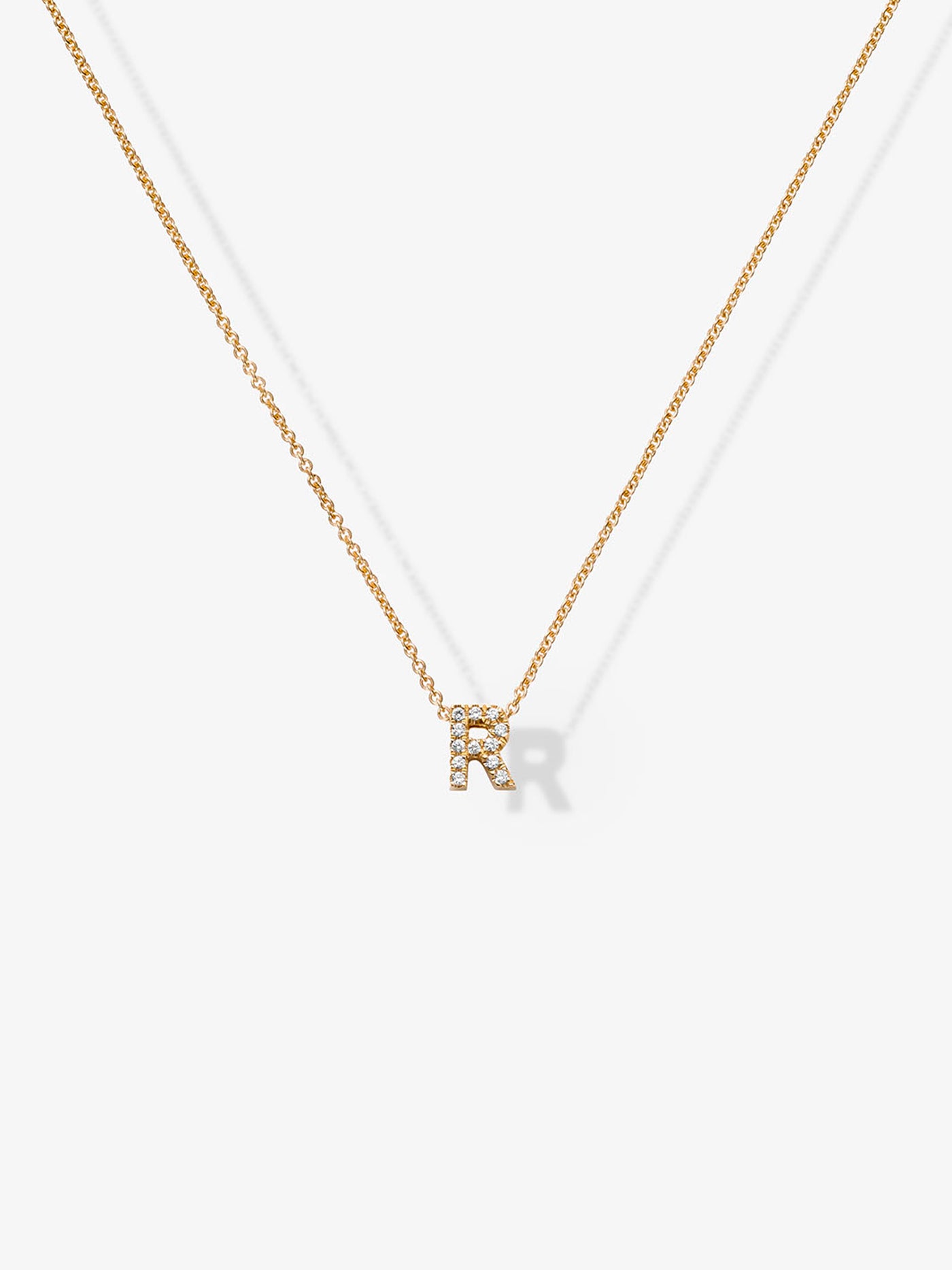 A delicate Letter R Necklace in Diamonds and 18k Gold features a pendant in the shape of the letter "R," adorned with small sparkling gemstones, and is shown against a plain white background.