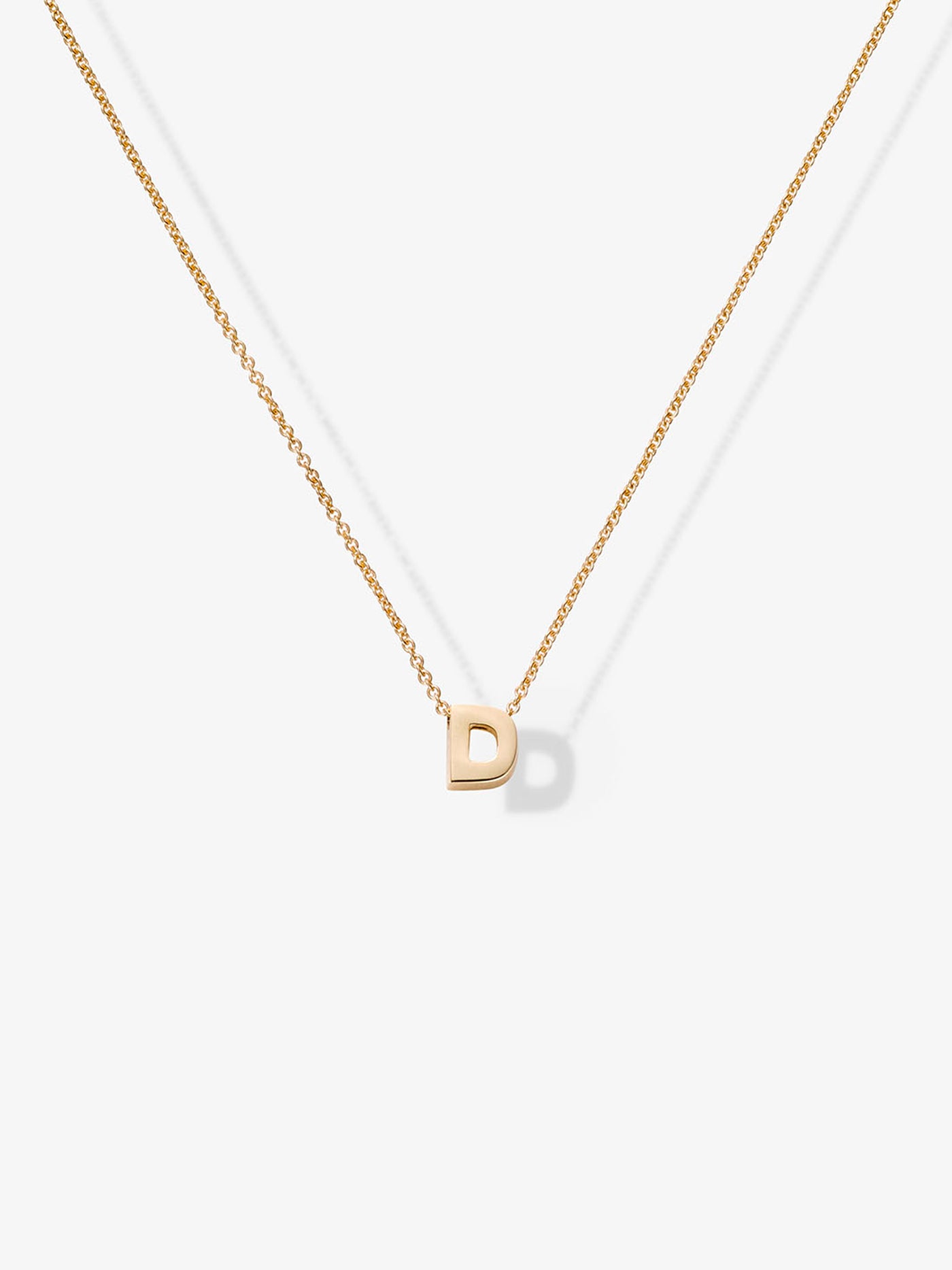 A delicate necklace named "Letter D Necklace in 18k Gold" features a small, customizable gold letter "D" pendant at its center, suspended from a fine chain. The minimalist design is set against a plain white background.