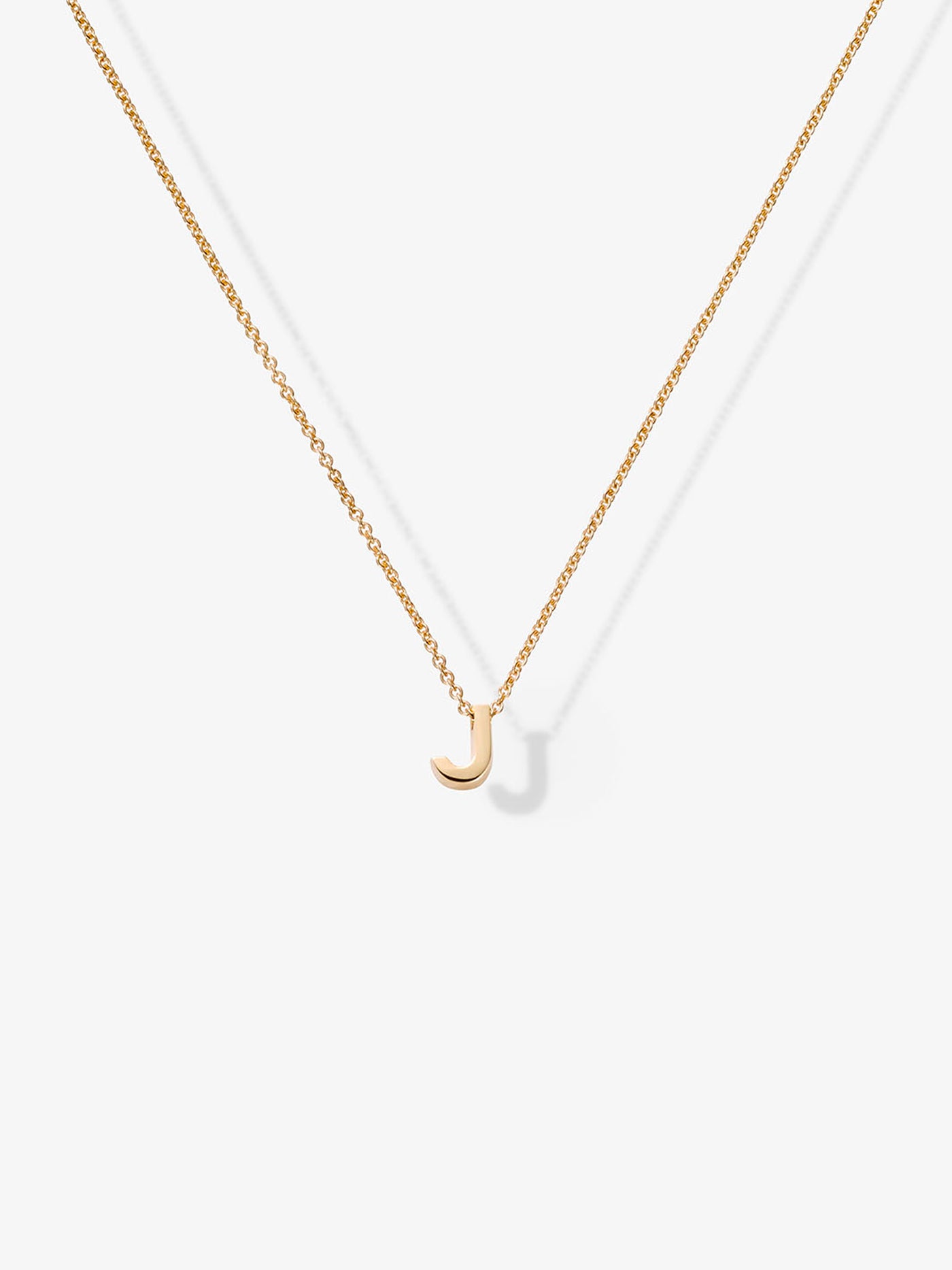 The Letter J Necklace in 18k Gold showcases a small, gold letter "J" pendant at its center, delicately hanging from a gold chain. Crafted from 18k solid gold, the necklace includes openable connectors for easy wear and is elegantly displayed against a plain white background.