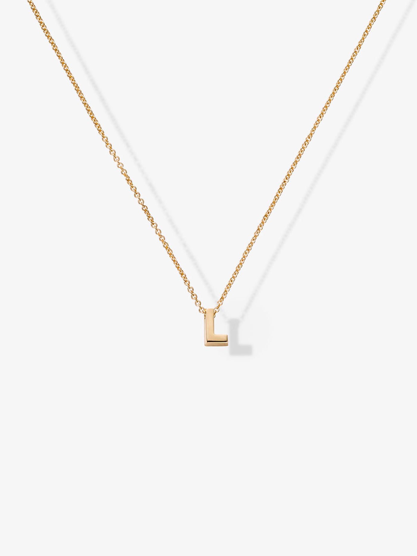 The Letter L Necklace in 18k Gold showcases a minimalist "L" shaped pendant at the center of a simple chain, set against a plain white background. The delicate 18k gold pendant features clean lines and a shiny finish, making it an elegant addition to any collection of charms.