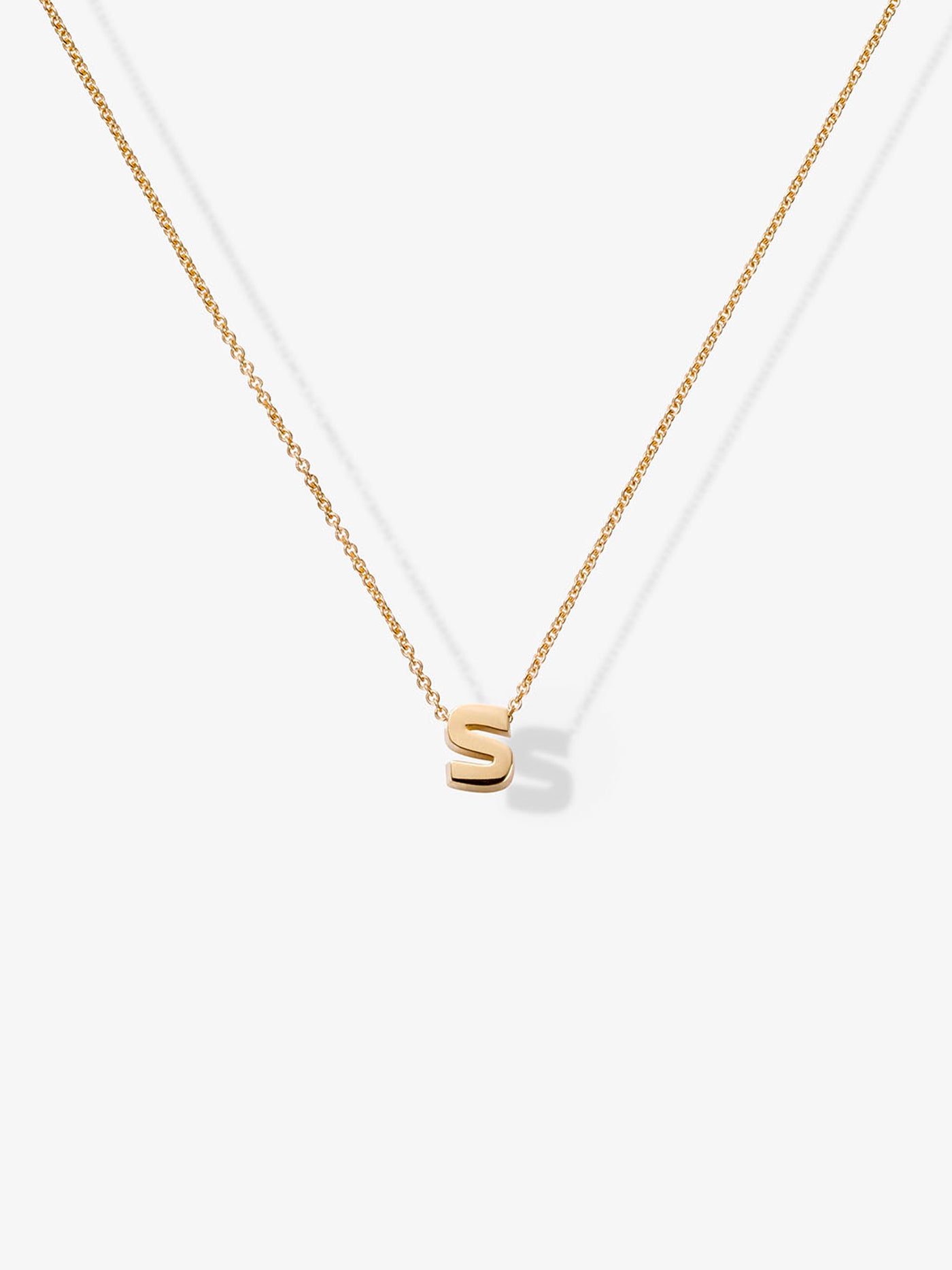 Product Description: The Letter S Necklace in 18k Gold features a delicate solid gold chain adorned with a small gold letter "S" pendant. Set against a plain white background, this exquisite piece highlights the simplicity and elegance of this refined necklace.