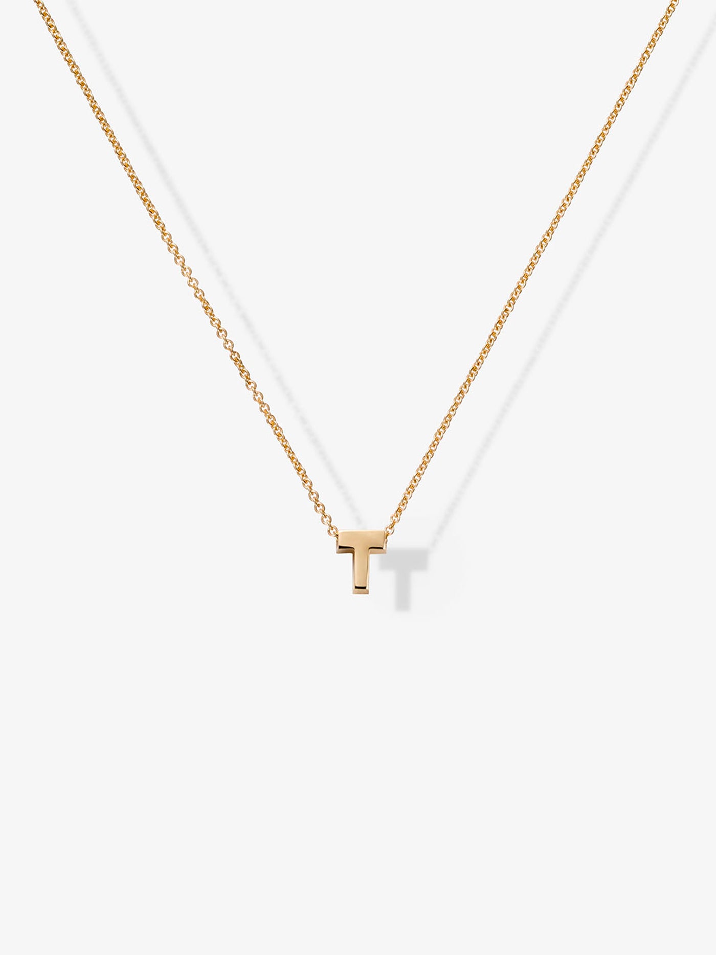 The Letter T Necklace in 18k Gold showcases a small, capital letter "T" pendant, elegantly suspended in the center of a fine chain. Its minimalist design and delicate 18k gold construction offer a modern and elegant look against the plain white background.