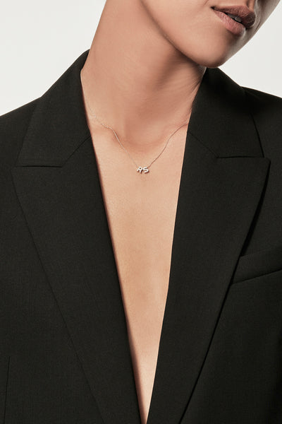 Close-up of a woman wearing a minimalist 18k gold initial diamond “S” "R" necklace  styled with a black blazer – personalised alphabet pendant jewellery