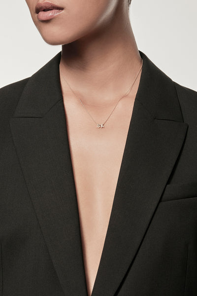 Close-up of a woman wearing a minimalist 18k gold initials “S” "K" necklace on a fine chain, styled with a black blazer – personalised alphabet pendant jewellery