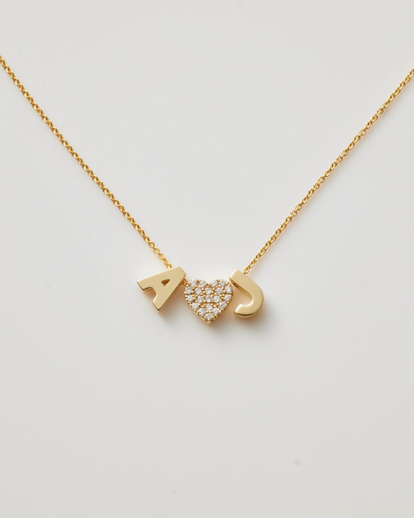 Small gold polished letter charms 'A' and 'J' paired with a diamond heart charm, threaded onto a delicate necklace chain.