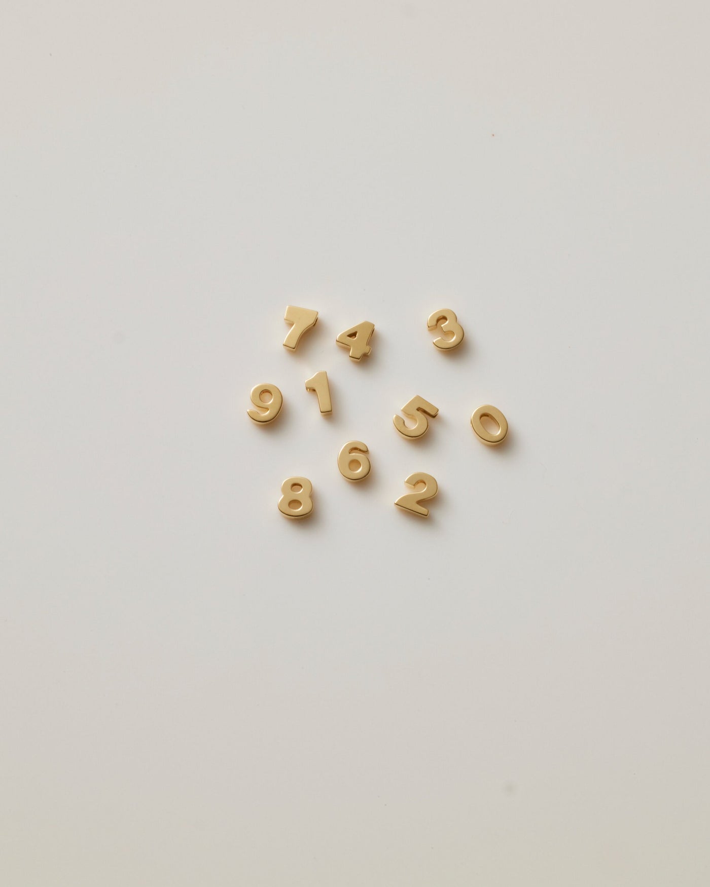 Small solid gold number charms (0-9), designed to slide onto a necklace chain for a personalised jewellery piece with symbolic meaning.