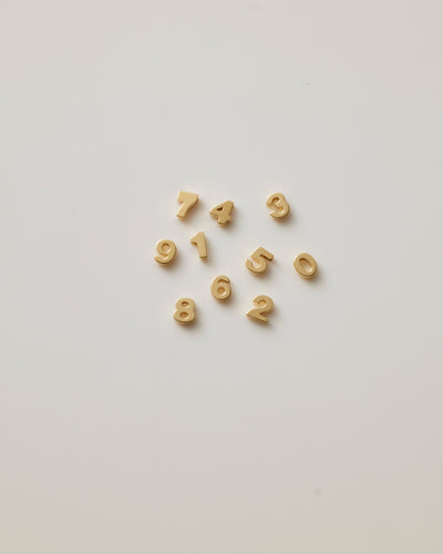 Small solid gold number charms (0-9), designed to slide onto a necklace chain for a personalised jewellery piece with symbolic meaning.