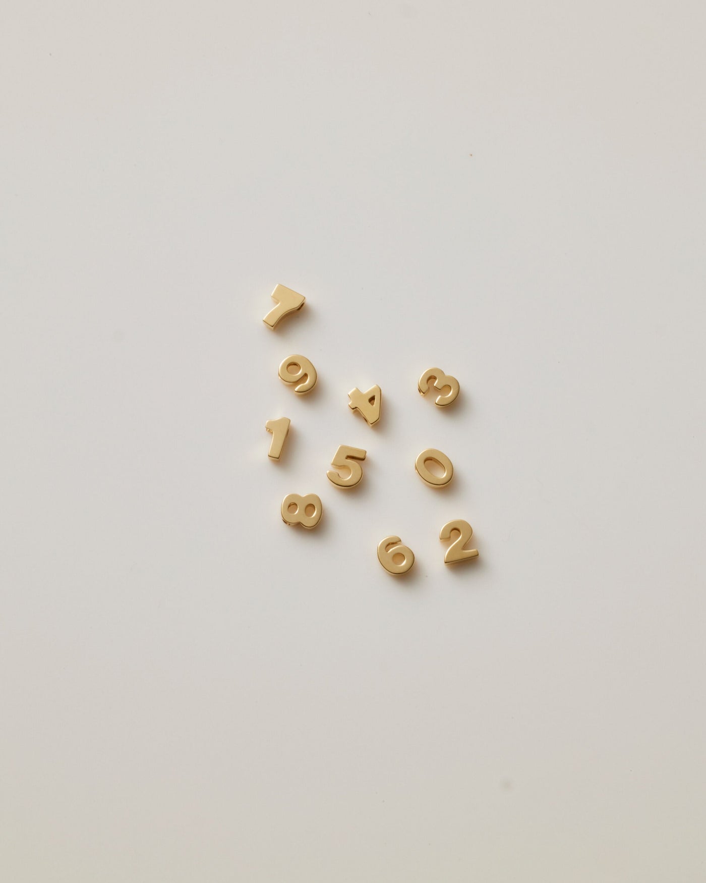 Small solid gold number charms (0-9), designed to slide onto a necklace chain for a personalised jewellery piece with symbolic meaning.