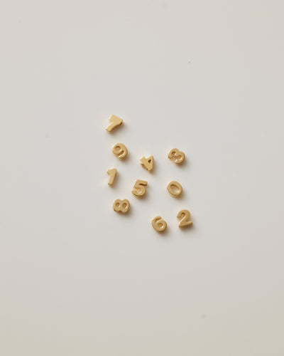 Small solid gold number charms (0-9), designed to slide onto a necklace chain for a personalised jewellery piece with symbolic meaning.